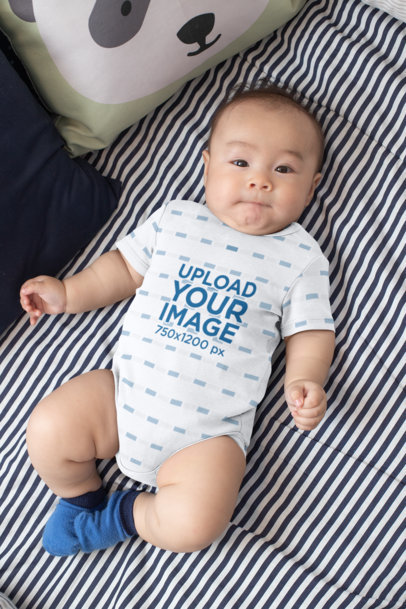 Mockup of a Baby Wearing a Onesie While Lying on a Bed  