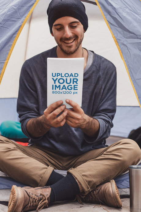 Book Mockup Featuring a Joyful Man Sitting in a Camping Tent 