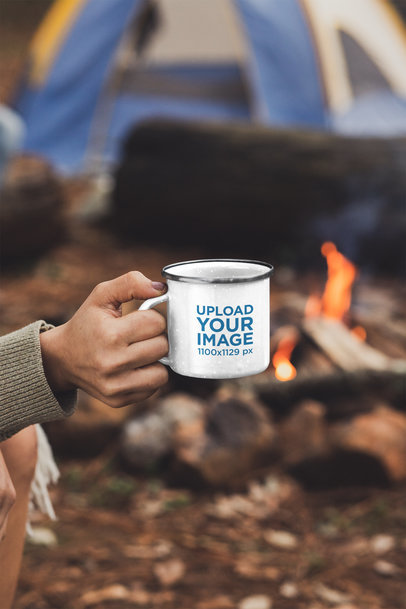  Mockup of a Woman Holding a 12 oz Enamel Mug by a Campfire