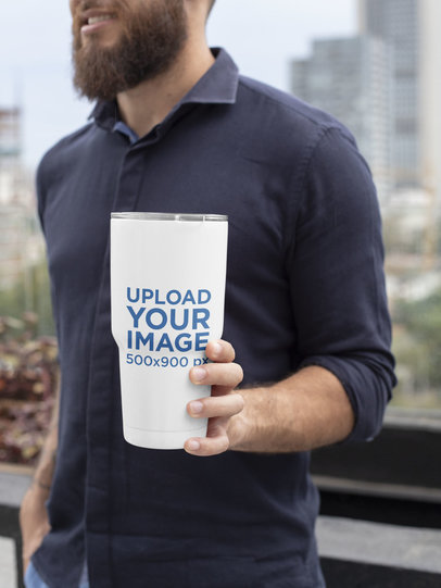 Mockup of a Bearded Man Holding a 30 oz Travel Mug in the City 30375
