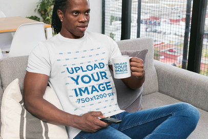 T-Shirt Mockup of a Man Holding an 11 oz Mug Sitting at Home