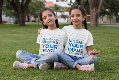 T-Shirt Mockup of Twin Girls Sitting on the Grass
