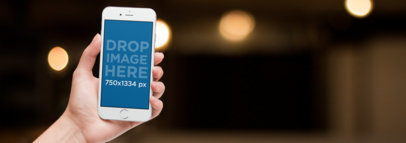 White iPhone Held Over a Blurred Lights Background Mockup