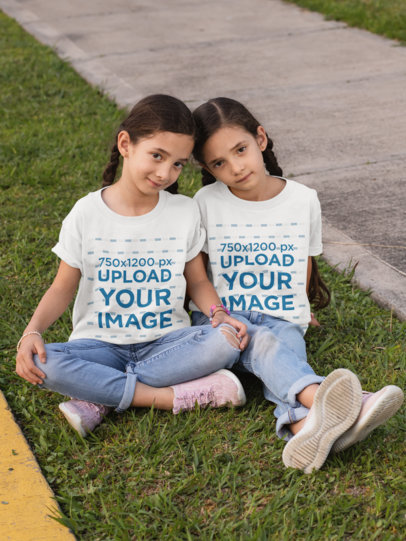 T-Shirt Mockup Featuring Twin Girls Sitting on the Grass 