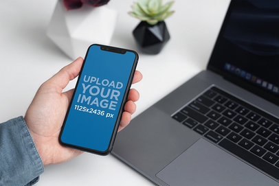 Mockup of a Man Holding an iPhone 11 in Front of a Computer