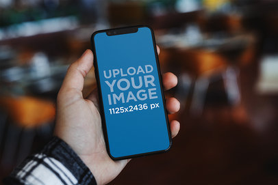 Mockup of a Man Holding an iPhone 11 Pro Against a Blurry Background 