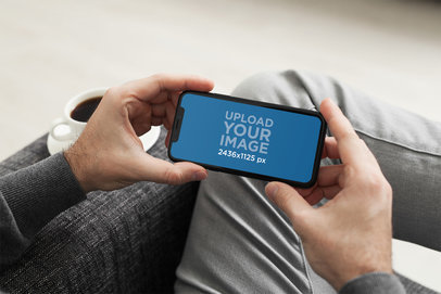 Mockup of a Man Holding an iPhone 11 Pro While Sitting on a Fabric Couch 2162-el1