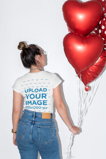 Back-View Mockup of a Woman Wearing a T-Shirt and Holding Heart-Shaped Balloons