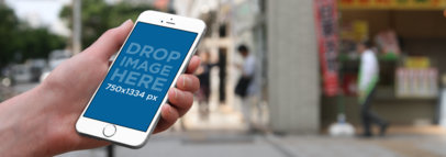 Mockup of a Man Holding an iPhone 6s Plus in the Street 