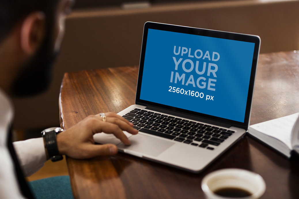 Mockup Featuring a Man Using His MacBook Pro on a Wooden Desk