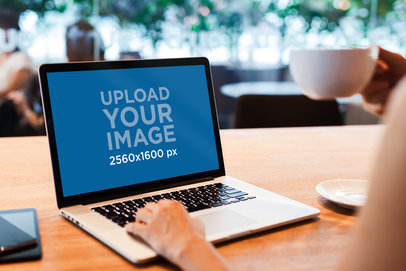 MacBook Pro Mockup Featuring a Person Holding a Coffee
