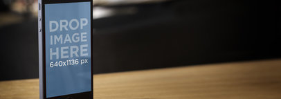  Mockup of an iPhone in Portrait Position Standing on a Wooden Table 