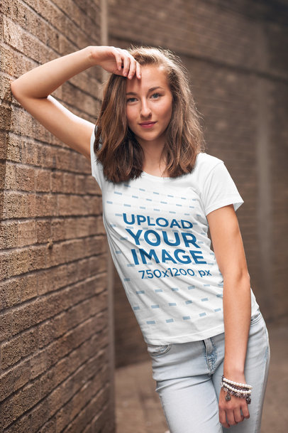 Mockup of a Young Woman Wearing a Customizable T-Shirt and Leaning Against a Brick Wall 