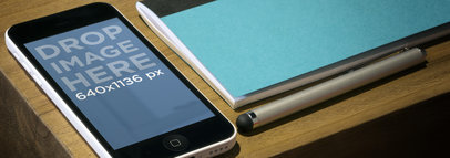 Mockup of an iPhone 5C in Portrait Position Placed By a Notebook 