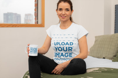 T-Shirt Mockup of a Middle-Aged Woman Holding an 11 oz Mockup and Sitting on Her Bed 