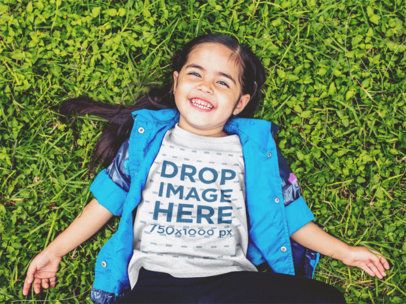 T-Shirt Mockup of a Little Girl Lying in the Grass Smiling