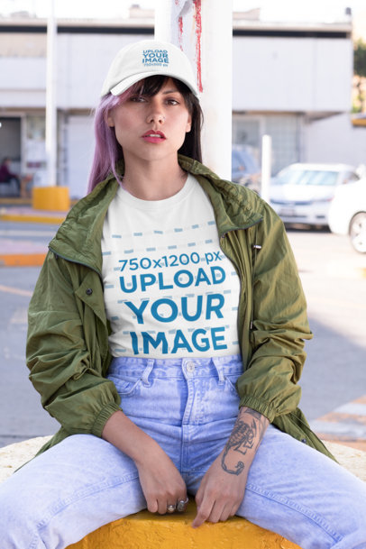 T-Shirt Mockup of a Tattooed Woman Wearing a Dad Hat and Sitting 