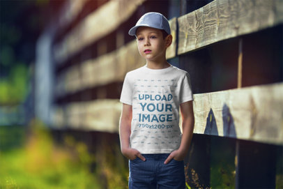 Mockup of a Boy Wearing a Customizable T-Shirt and Standing by a Wooden Fence 
