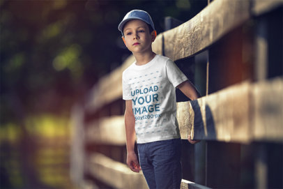 T-Shirt Mockup Featuring a Serious Boy by a Rustic Wooden Fence 