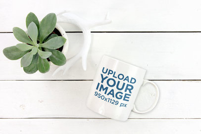 Mockup Featuring an 11 oz Mug Lying on a White Wooden Table by a Succulent 