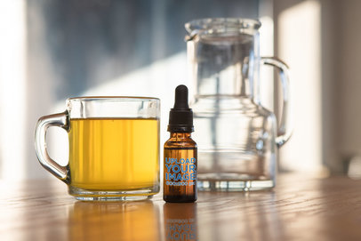 Mockup of a Dropper Bottle Placed Next To a Cup of Tea