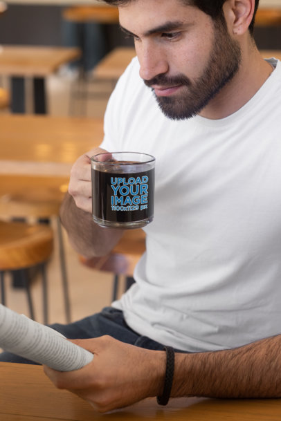 Mockup Featuring a Man Holding a Clear Glass Mug While Reading 