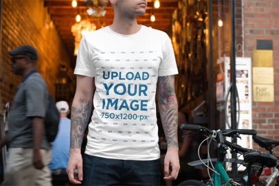 T-Shirt Mockup of a Tattooed Man Standing Next to a Bike