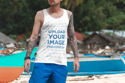 Tank Top Mockup of a Tattooed Man Standing by Some Boats at the Beach