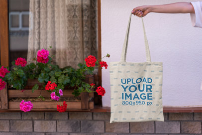 Mockup of a Tote Bag Against a Window with Flowers 