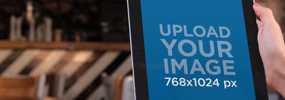 Mockup of a Woman Holding an iPad in Portrait Position at a Restaurant