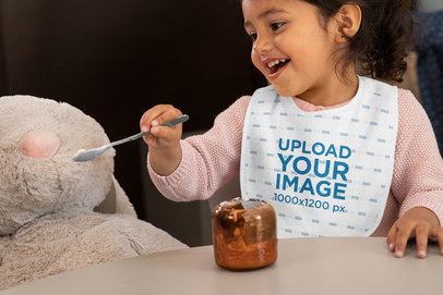 Bib Mockup Featuring a Little Girl Feeding a Stuffed Animal 