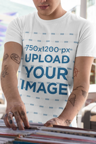 T-Shirt Mockup Featuring a Man with Tattooed Arms at a Music Store