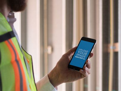 Mockup of a Man Holding an iPhone in Portrait Mode on a Construction Site
