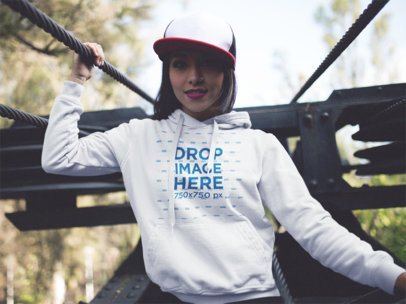 Hoodie Mockup of a Young Woman Wearing a Hat Outdoors