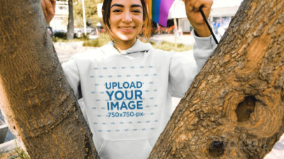 Pullover Hoodie Video Featuring a Happy Woman Holding a Small LGBT Pride Flag by a Tree