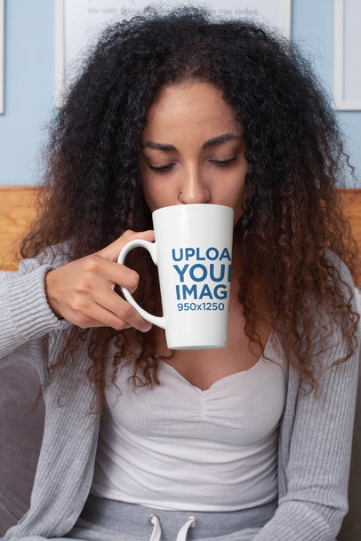 Mockup of a Woman Drinking From a 15 oz Conical Coffee Mug While Sitting on a Bed 