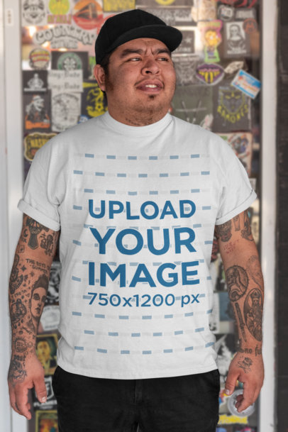 Tee Mockup of a Man with Tattooed Arms Posing by a Glass Door 