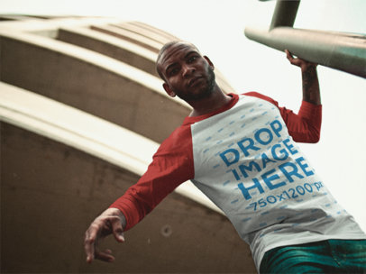 Young Black Man Wearing a Raglan Tee Mockup While Looking Down Near a Building a12562