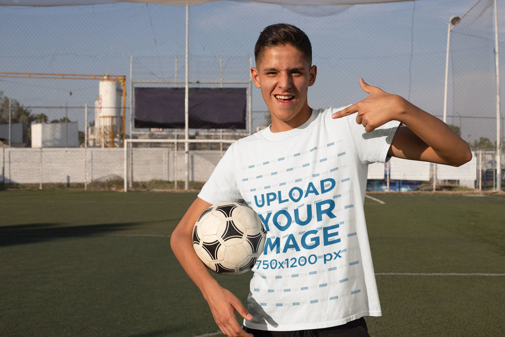 Mockup Featuring a Teenager With a Soccer Ball Pointing at His T-Shirt 