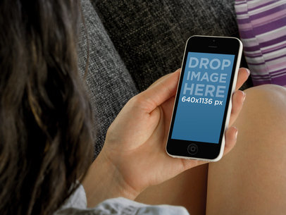 iPhone 5c Mockup Featuring a Young Woman Sitting on a Fabric Couch 