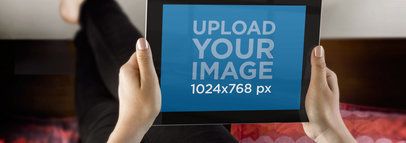 Mockup of a Woman Holding an iPad While Resting on a Bed  a