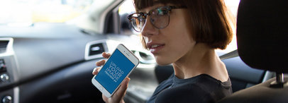Lovely Girl Riding in the Frontseat of a Car Holding an iPhone 7 in Portrait Position Mockup a12942wide