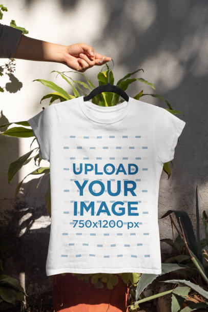 Mockup of a Woman's Hand Holding a T-Shirt by Some Garden Plants 33866