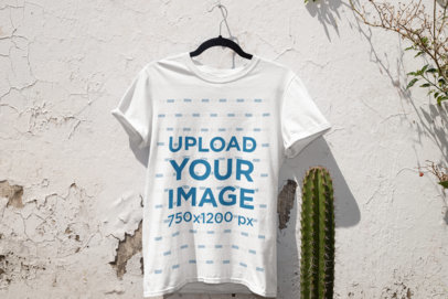 Mockup of a T-Shirt Hanging on a White Wall by Some plants