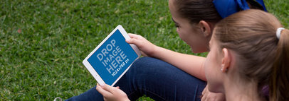 Two Girls Playing with a White iPad Mini Mockup in Landscape Position in their Garden