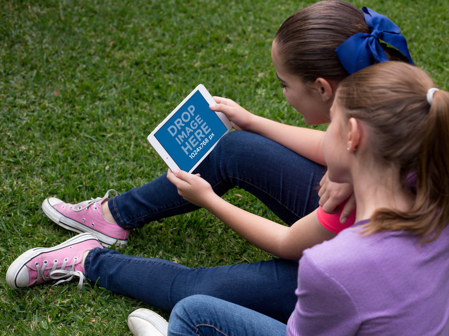 Mockup of Two Women Playing with a White iPad Mini in Landscape Position in their Garden