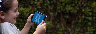 Mockup of a Little Girl Playing on a Black iPhone 7 Plus in Landscape Position in the Back Yard
