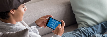 Teenager Sitting on a Couch and Playing on his Black iPhone 7 Plus in Landscape View Mockup a13034wide
