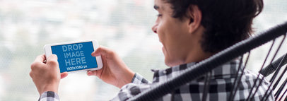White iPhone 7 in Plus Landscape Position Mockup Featuring a Young Man Playing in a Chair