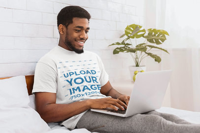 T-Shirt Mockup of a Man Using a Laptop in His Bedroom 